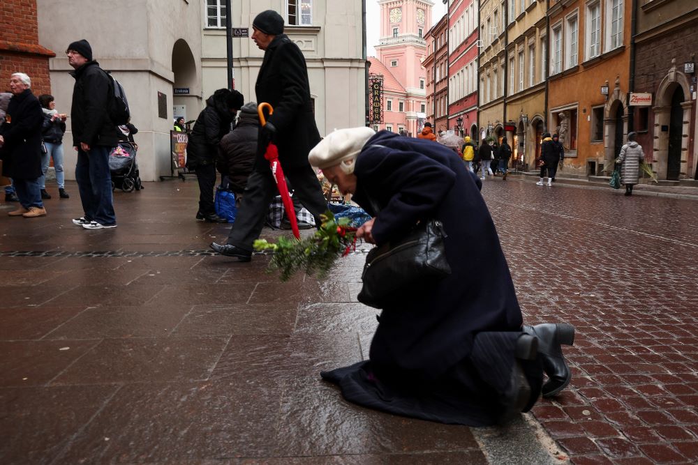A woman kneels in front of the cathedral in Warsaw, Poland, on the anniversary of St. John Paul II's death April 2, 2023.